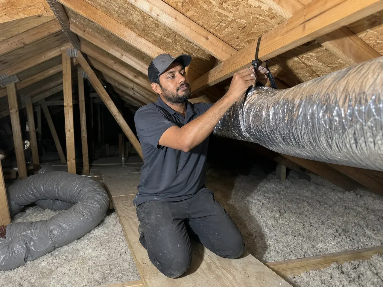 ECHA HVAC technician strapping a new run of insulated flex duct to a truss in a Sacramento-area attic